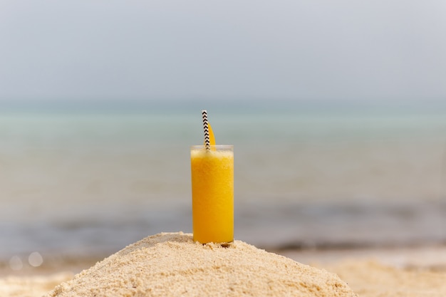 Cold multi fruit cocktail drink with slices of mango on beach background