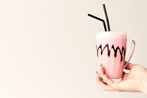 Cold pink milkshake in glass mug on. Cocktail holds female hand. Minimalism. Place for text.