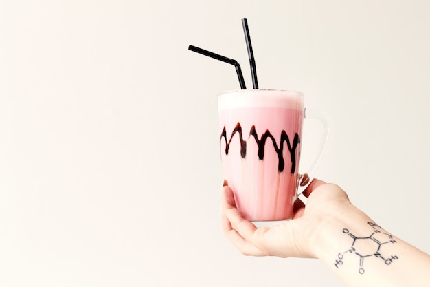 Cold pink milkshake in glass mug on. Cocktail holds female tattoo hand. Minimalism.