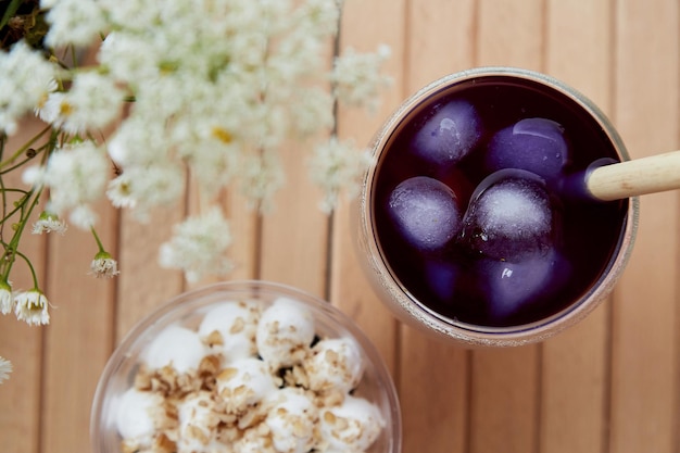 Cold purple anchan cocktail with antioxidants straw reed and vegan gluten free nuts dessert in a disposable cup Chamomile flowers blurred foreground on the wooden table