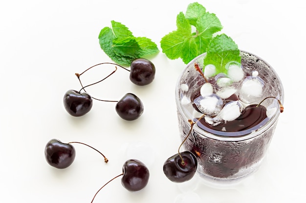 Cold refreshing detox water with cherry, mint and ice cube in glass.