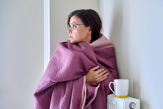 Cold season woman with plaid mug of hot tea warming near wall heating radiator