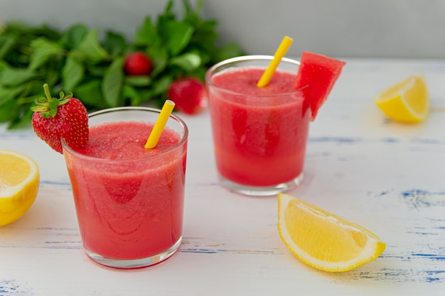 Cold watermelon smoothie with mint, lemon and strawberries in glasses . Colorful refreshing drinks for summer