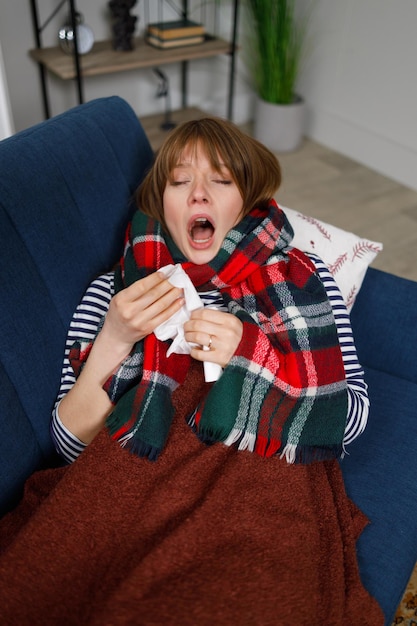 Cold woman lying on the sofa at home sneezes into a paper handkerchief