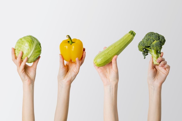 Collage with female hands holding cabbage pepper zucchini broccoli on white background