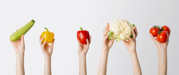 Collage with female hands holding zucchini pepper cauliflower tomato on white background Banner