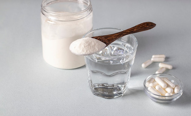 Collagen powder in spoon on glass of water, collagen capsules and jar of powder on a light background. Healthy and anti-aging concept.