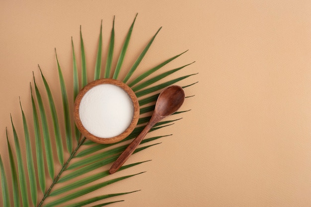 collagen powder in a wooden bowl, spoon, peach space, top view, green leaf