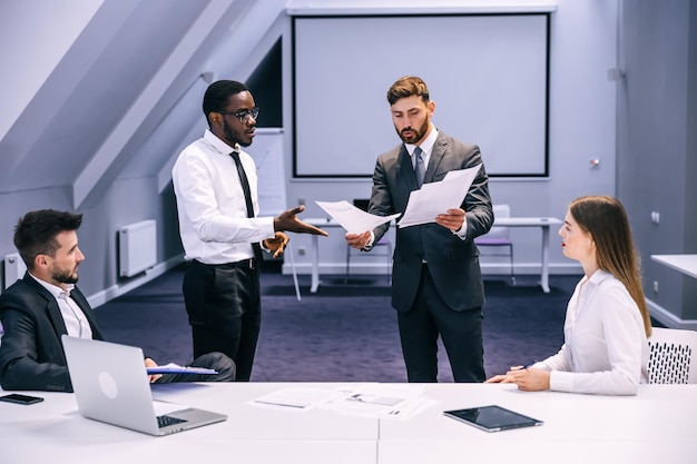 Colleagues argue at corporate office meeting crazy employees quarreling shouting conflict at work racial hatred harassment concept