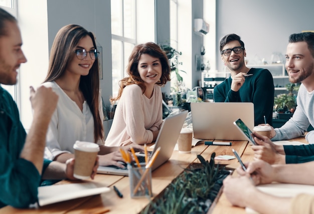 Colleagues become friends. Group of young modern people in smart casual wear discussing something and smiling while working in the creative office