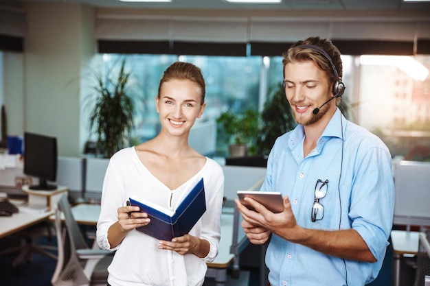 Colleagues smiling speaking holding tablet and notebook over office background