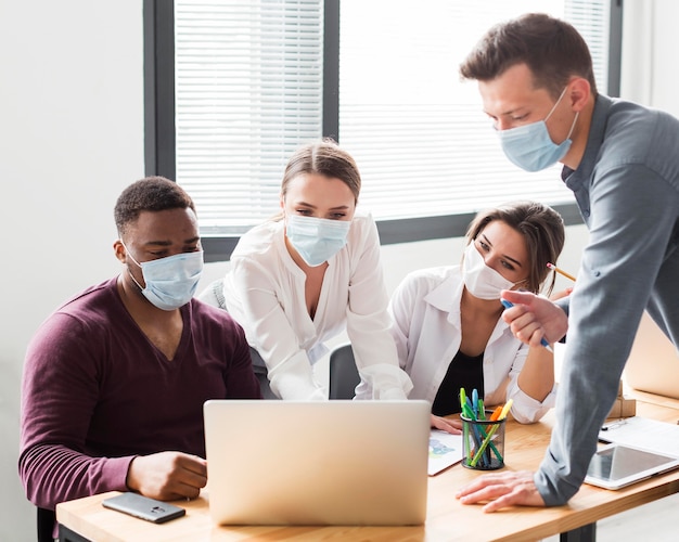 Colleagues at work in the office during pandemic looking at laptop with masks