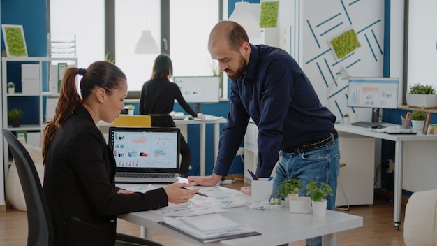 Colleagues working on data charts design with laptop and papers for business planning and marketing strategy at corporate job. People doing teamwork for industry development at company