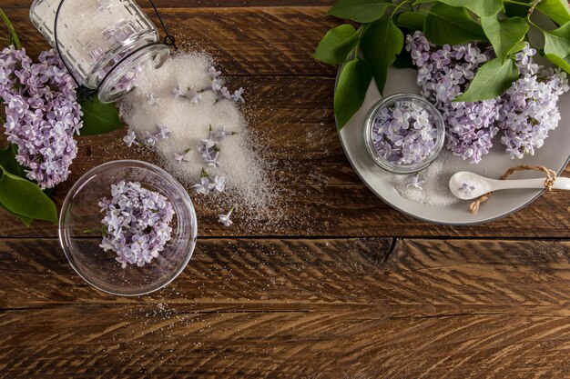 Collected lilac flowers in a bowl in a plate and sugar in a jar to make lilac sugar from flowers top view wooden background