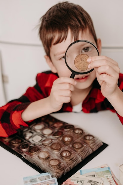 collecting coins The boy examines an old coin through a magnifying glass Dollars euros on the table Money of different nations Savings in the form of currencies and coins