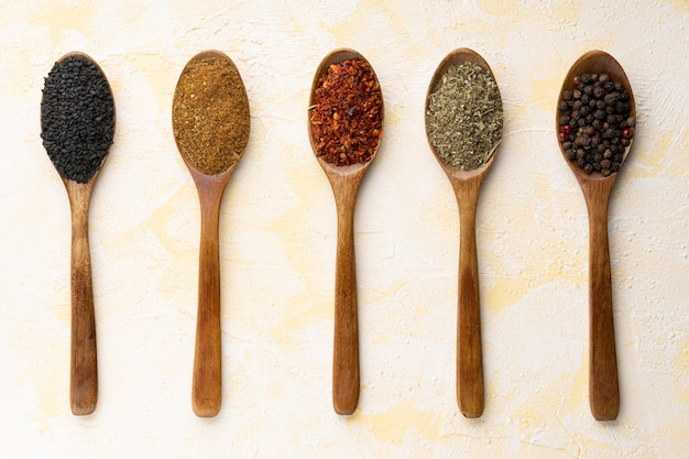 Collection of five spices on wooden spoons on yellow cement surface.