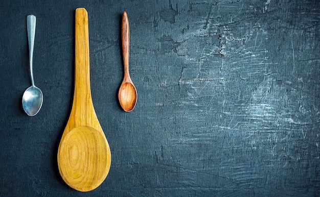 Collection of large wooden spoons with small and stainless steel spoons on black background top view