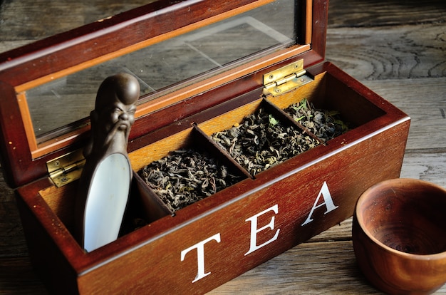 Photo a collection of tea in a wooden box, a wooden glass with a stylized teaspoon on a wooden background.