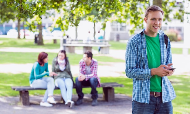 College boy text messaging with blurred students in park