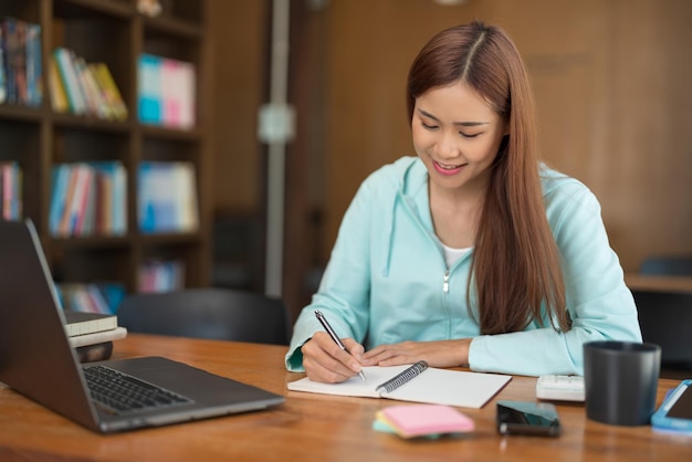 College education concept Teenage girl watching video tutorial of tutor on laptop and taking notes