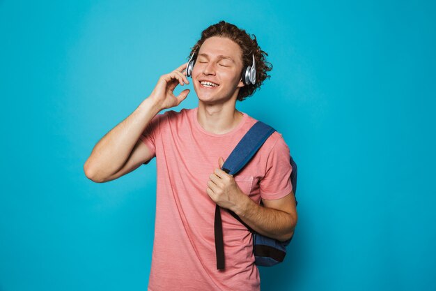 College man with curly hair wearing backpack listening to music via headphones