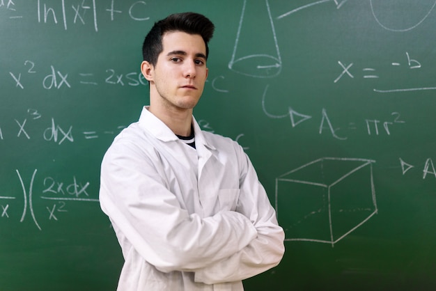 College student in laboratory class. College student with white coat, standing in front of chalkboard.