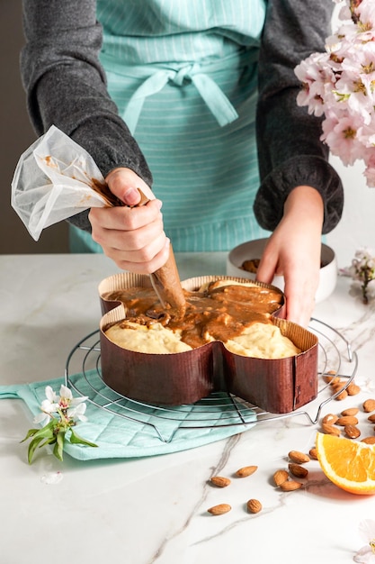 Colomba - traditional italian easter dove cake, process of decorating with hazelnut based glaze, macaranage, sprinkling with almonds,  woman shef hands.