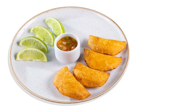 Colombian empanadas with spicy sauce and lemon wedges on a plate top view