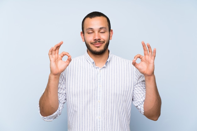 Colombian man over isolated blue wall in zen pose