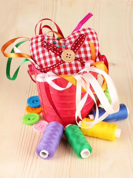 Color bucket with multicolor ribbons and thread on wooden background