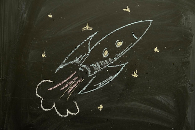 Color chalk hand drawn illustration of rocket on black chalkboard background Copy space