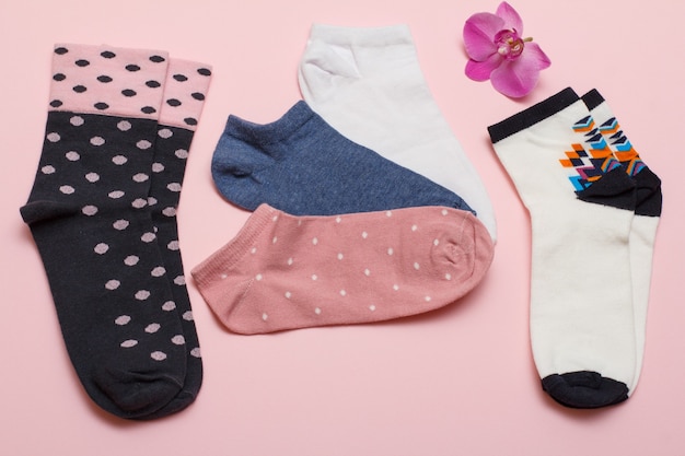 Color pairs of women socks and orchid flower on pink background, Top view.