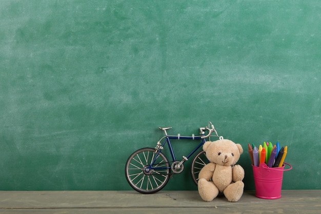 Colored crayons and toy bear on the wooden table elementary school education concept chalkboard background