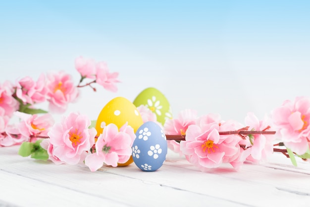 Colored eggs with pink flowers on white wooden surface.