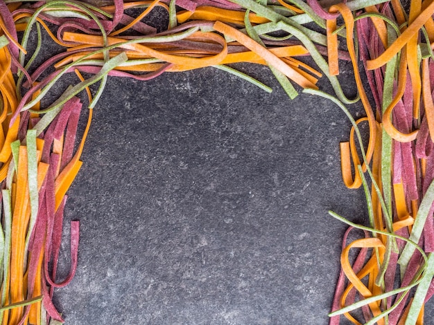 Colored fresh raw uncooked homemade pasta tagliatelle green spinach pink beetroot and yellow carrot with flour over grey marble background Top view Food background