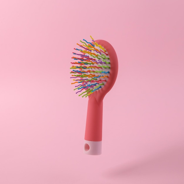 Colored hairbrush levitating on pink background with shadow Minimal beauty still life