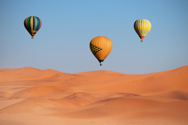 Colored hot air balloons flying over the sand dunes at sunset