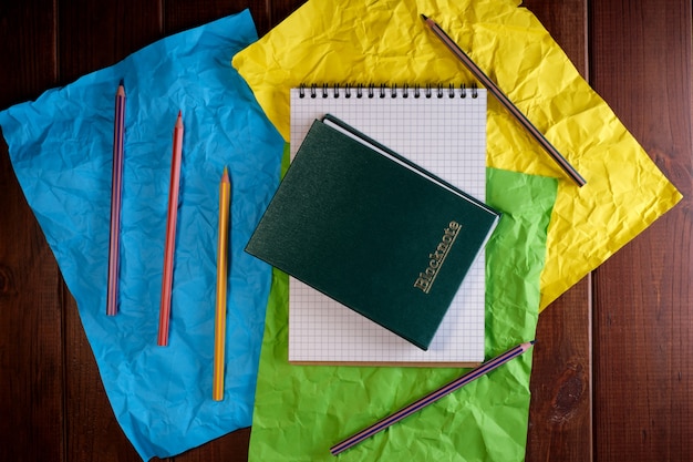 Colored paper background from crumpled sheets with notepad and pencils on dark wooden table top