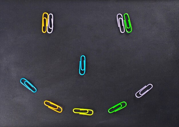 Photo colored paper clips on a chalkboard background in the form of a smile face school and education