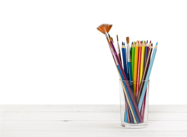 Colored pencils and brushes to draw in glass on light wooden background