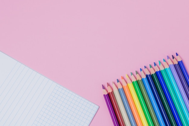 Colored pencils and a school notebook on a pink background