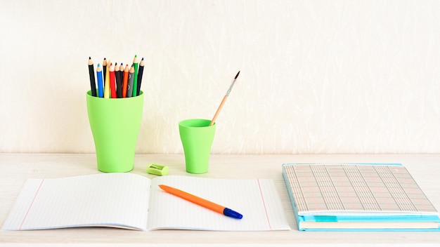 Colored pencils in a stand a notebook a pen and a textbook on a wooden table