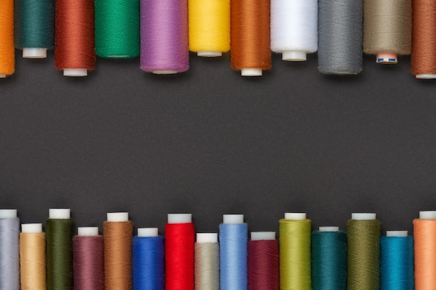 Colored sewing threads are laid out on a gray background space for text