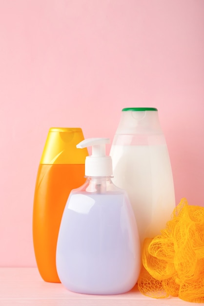 Colored shower gel bottles and sponge on pink wall. Top view