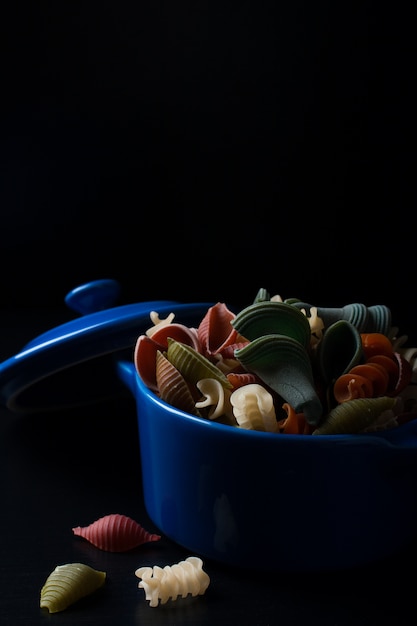 Colored spelt pasta in blue ceramic pot 