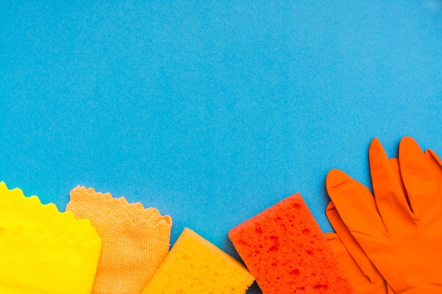 Colored sponges for washing dishes, microfiber rags and rubber gloves lie in a row against a blue background. Cleaning Tools Concept. Copy space