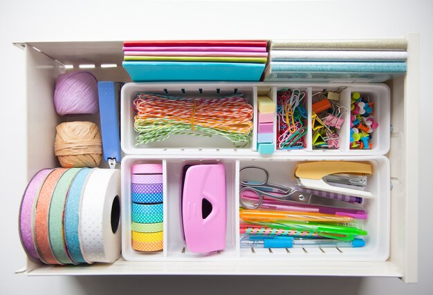 Photo the colored stationery is neatly arranged in white containers in the drawers of the nightstand. storage and tidying up the workplace.