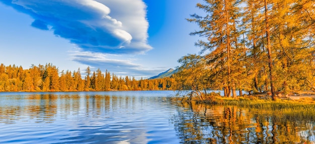 Colorful autumn sunrise clouds sky over lake. Panoramic nature landscape, peaceful dream water