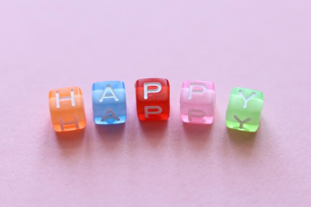 colorful beads spelling the word happy on a pink background