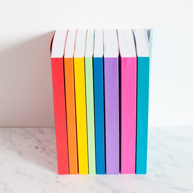 Photo colorful books are outlined in the colors of the rainbow. stacked of the books on a shelf near the white wall